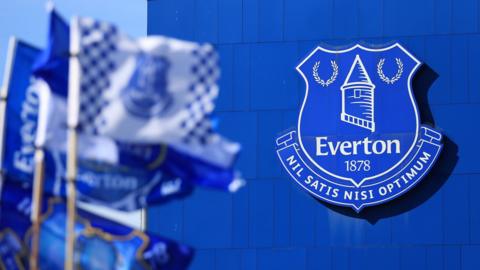 Everton badge on the side of Goodison Park, with club flags in the foreground