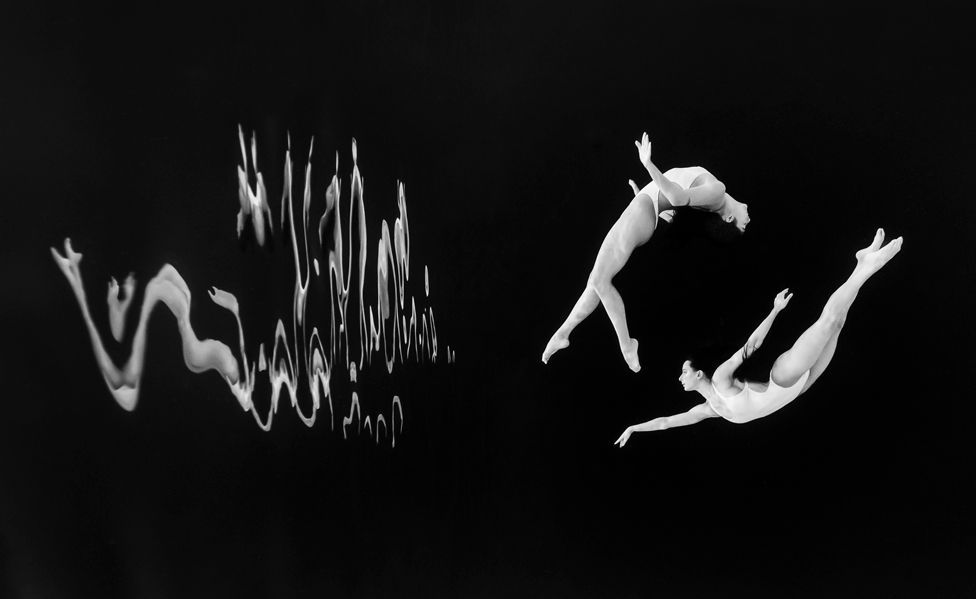 Synchronised swimmers pose for an underwater portrait in front of a black background