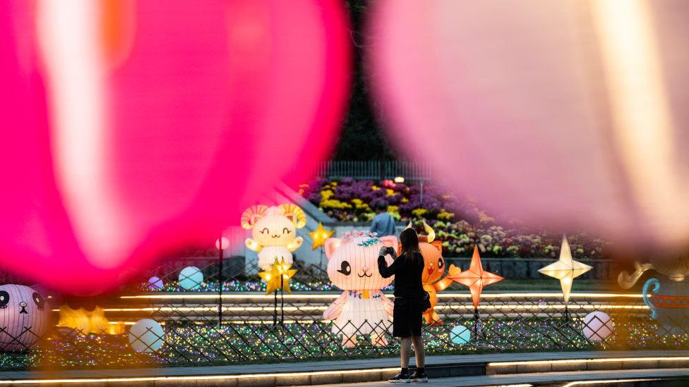 A woman takes pictures of colourful lanterns set up at Hong Kong Velodrome Park
