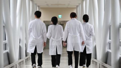 A group of doctors walk with their backs turned down a hospital corridor in Seoul