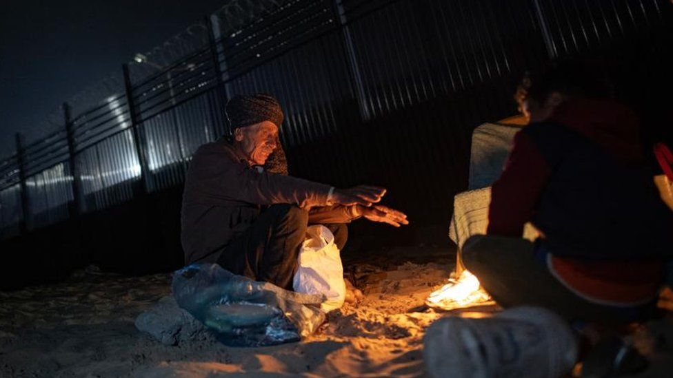 An elderly man sits in front of a fire outside a tent in the city of Rafah, in the southern Gaza Strip 27 February 2024.