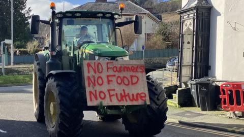 Farmer in tractor with a plaque saying "No farmers, no food, no future"