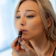 Woman putting on lipstick in mirror thumbnail