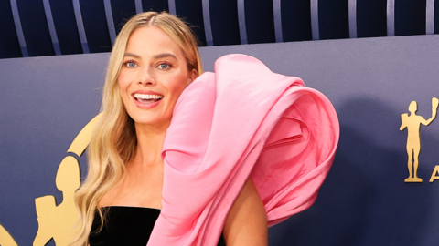 Margot Robbie smiling at the Screen Actors Guild Award, wearing a black and pink outfit